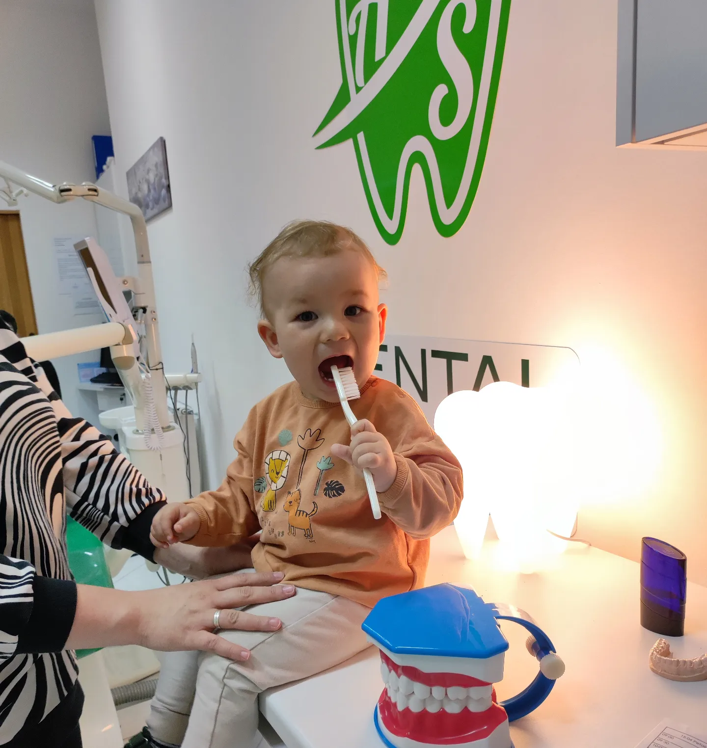 Malo dijete uči prati zube velikom četkicom u ordinaciji AS Dental, uz mamu koja ga pridržava